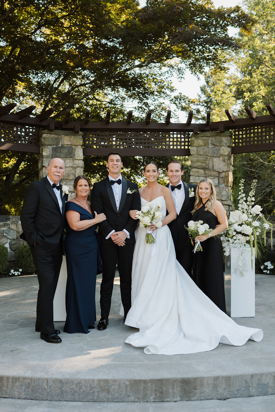 Bride and groom posing for a warm family portrait in front of a stone ceremony structure.